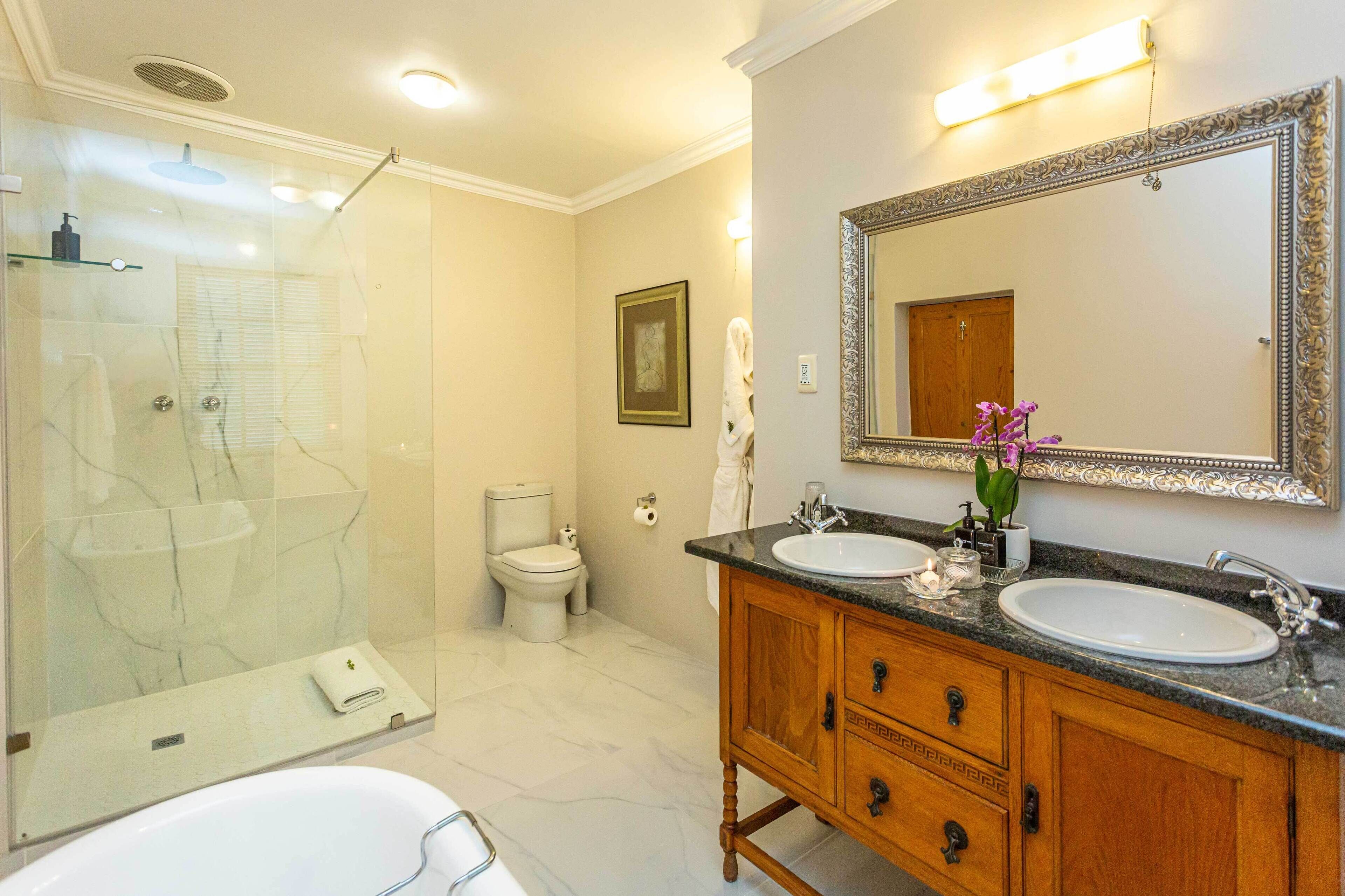 A bathroom with two sinks, a large mirror, a shower, and a toilet.