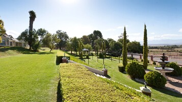 A well-maintained garden with a lawn, hedges, and a fountain. There are tall trees and a building in the background.