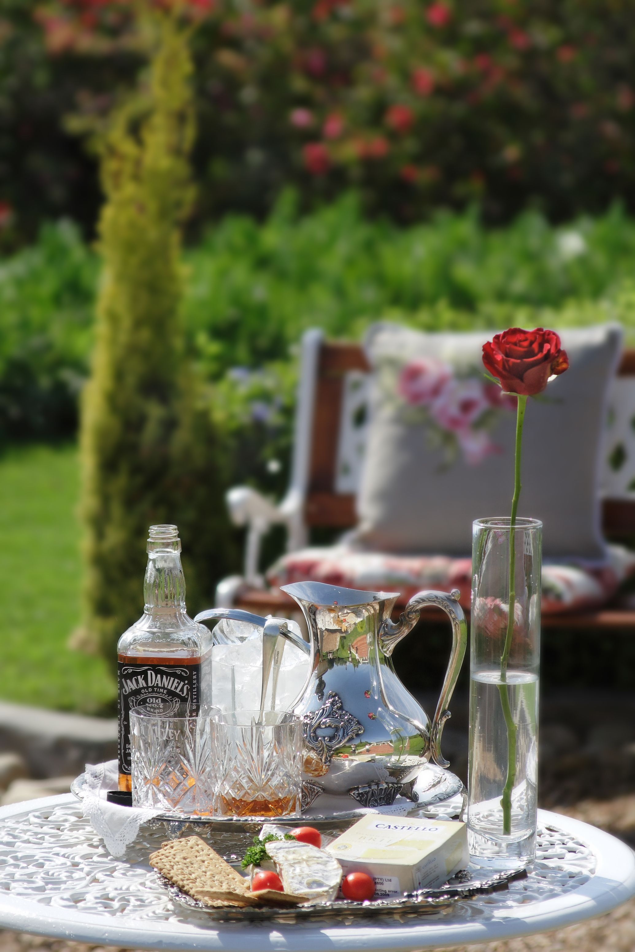 Mesa al aire libre con jarra, botella, vaso y rosa.
