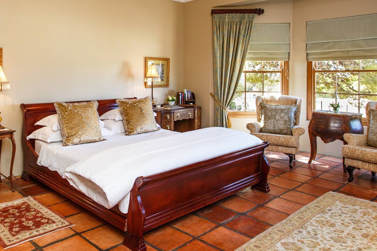 A bedroom with a wooden bed, two bedside tables, a chair, a desk, and a window with curtains.