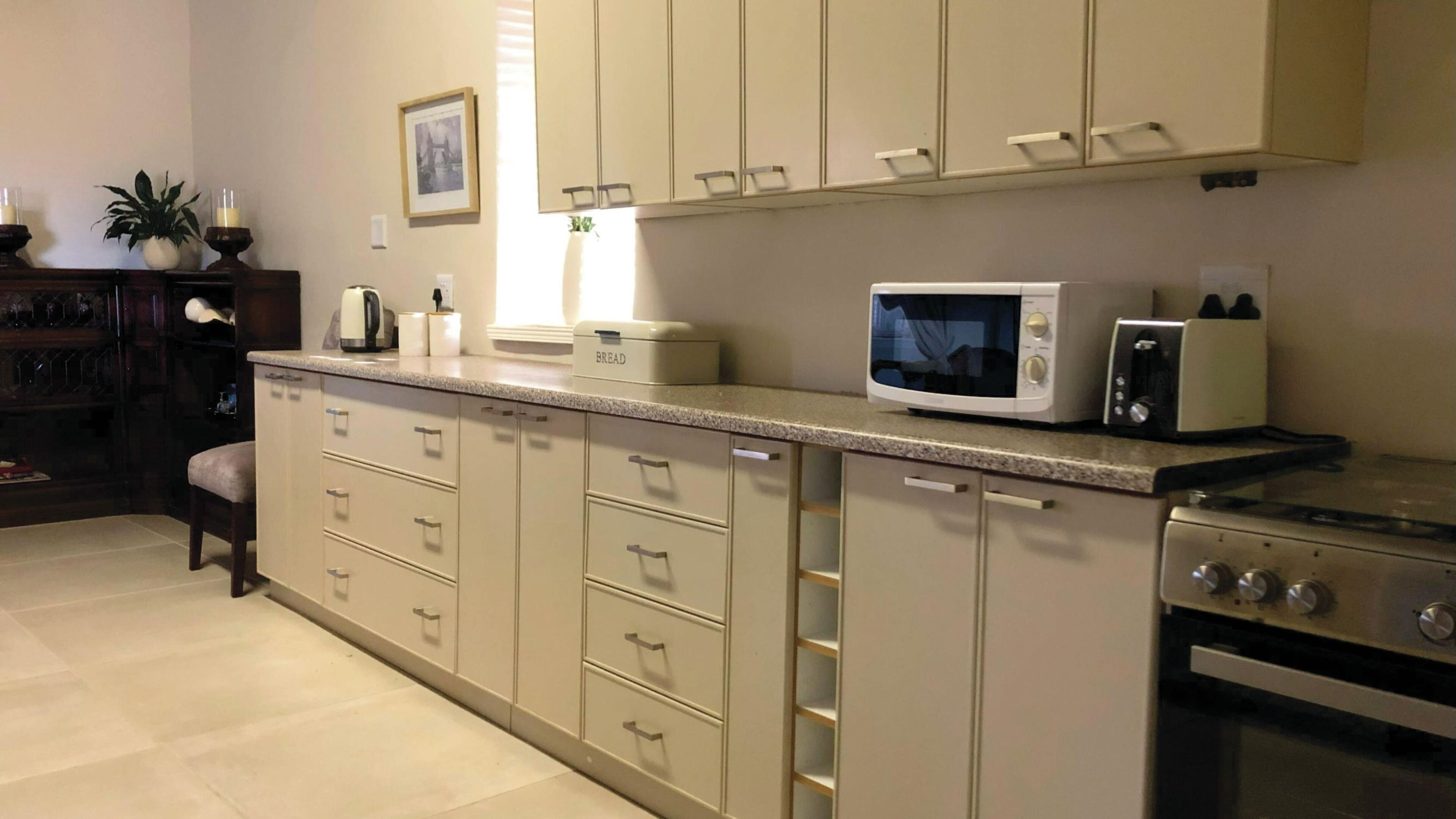 A kitchen with a microwave, toaster, and a bread box on the counter. There are cabinets with drawers and a stove.