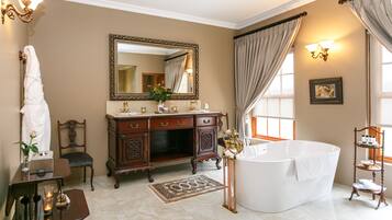 Un baño amplio con una bañera independiente, un espejo grande y un tocador con un mueble con detalles dorados.