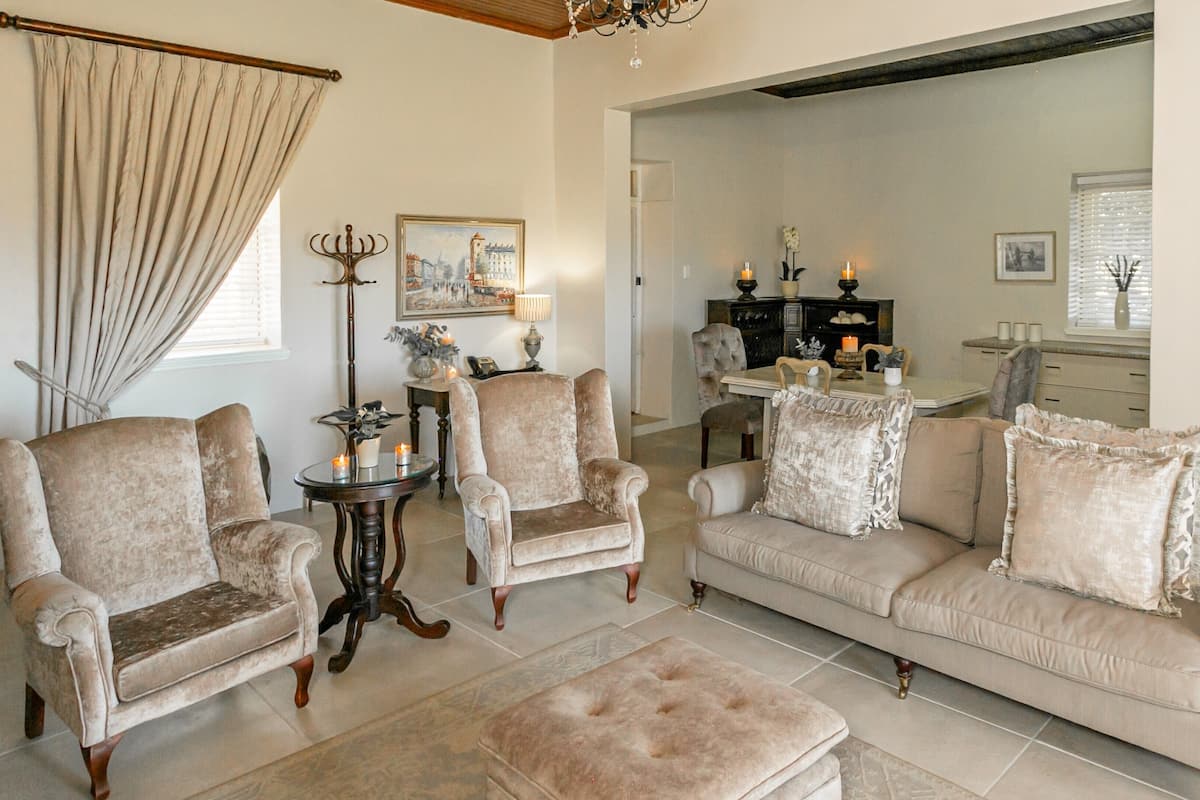 A living room with a sofa set, two armchairs, a coffee table, and a side table with candles. There is a painting on the wall and a chandelier above the sofa.