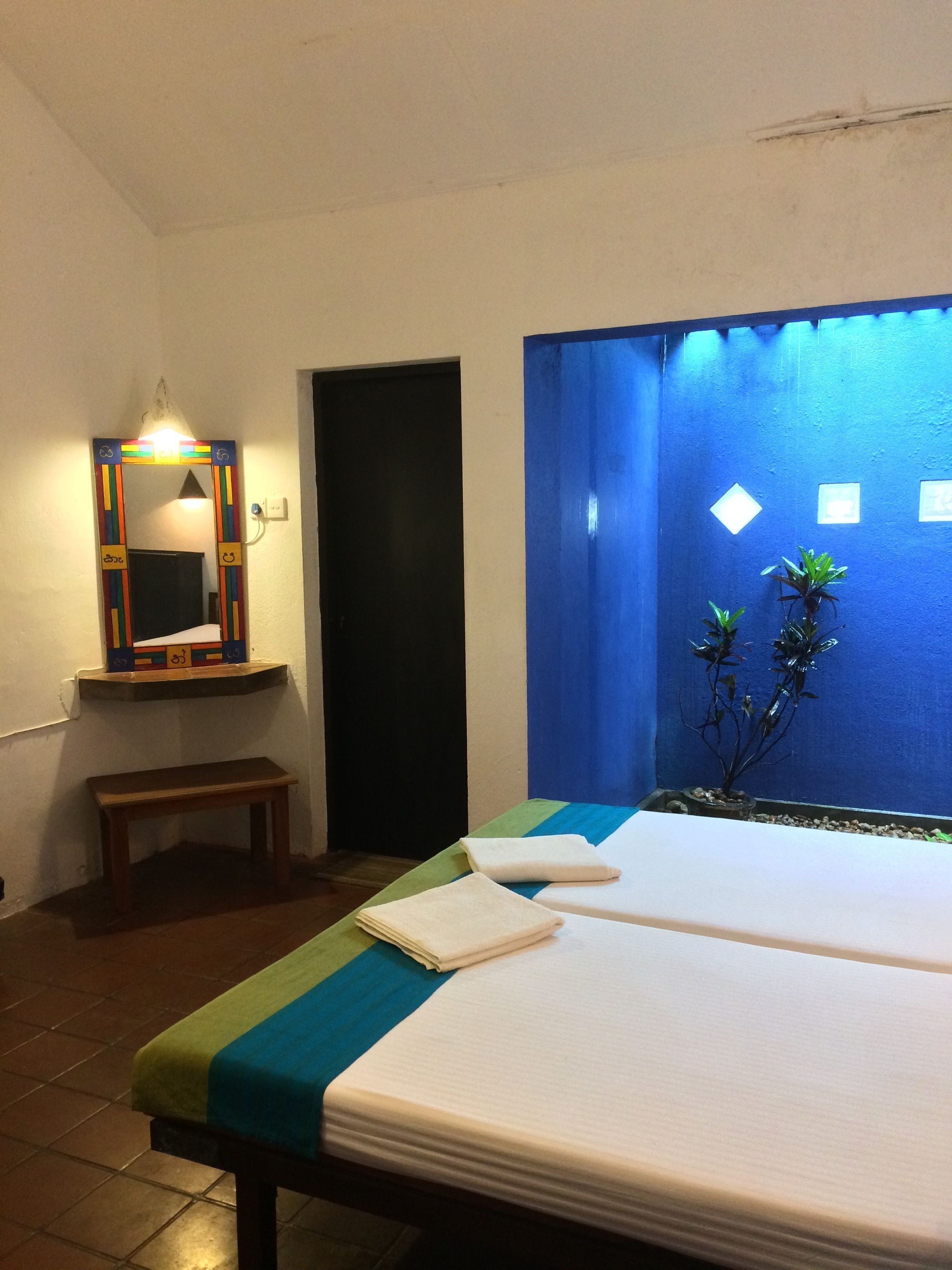 A hotel room with a bed, a bench, a mirror, and a blue wall with a window.