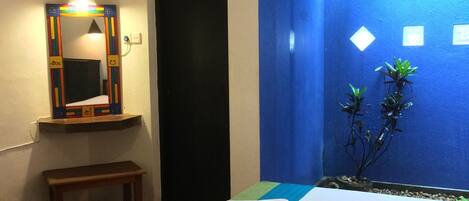 A hotel room with a bed, a bench, a mirror, and a blue wall with a window.