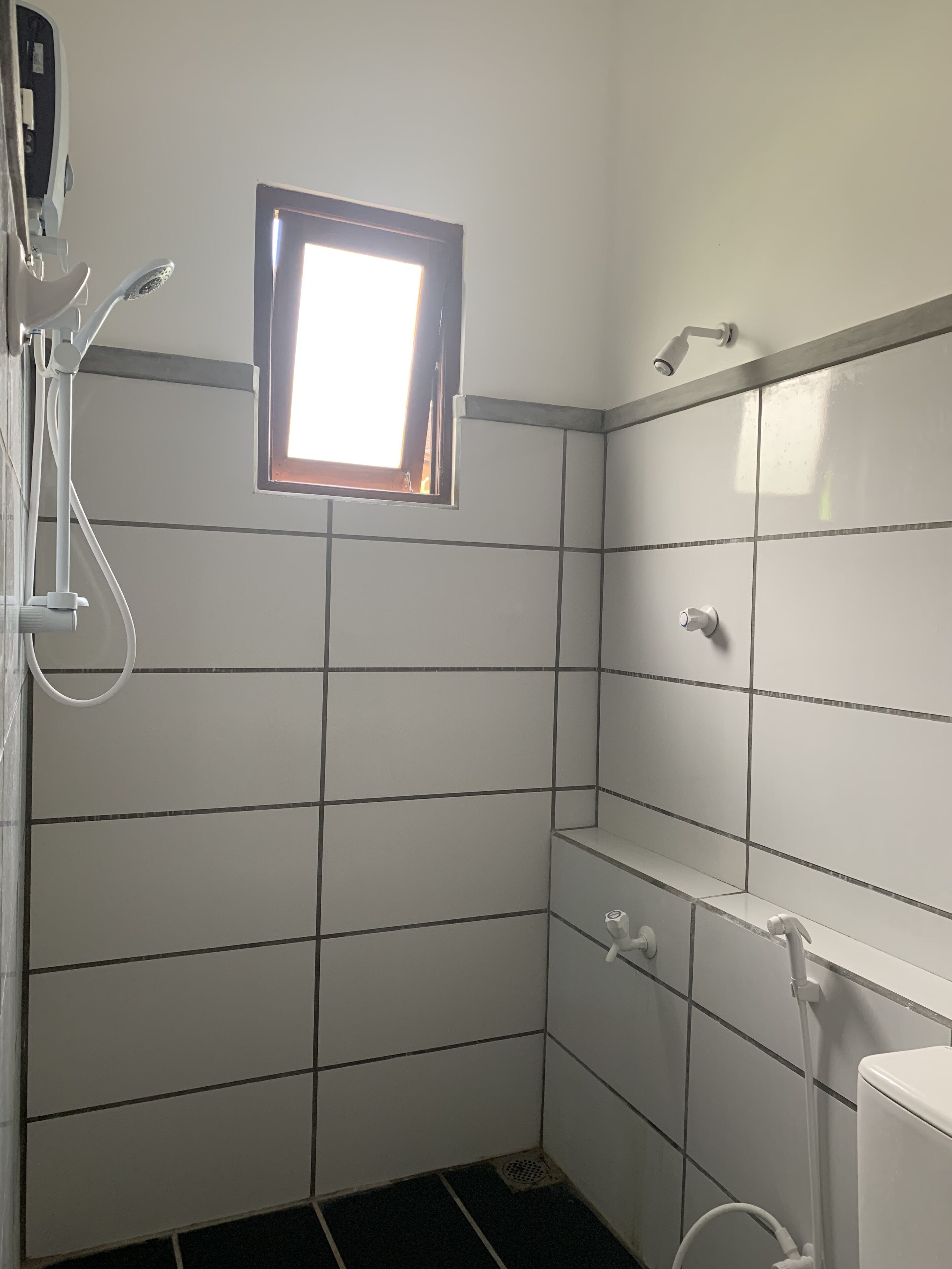 A bathroom with white tiled walls, a window, a shower, and a toilet.