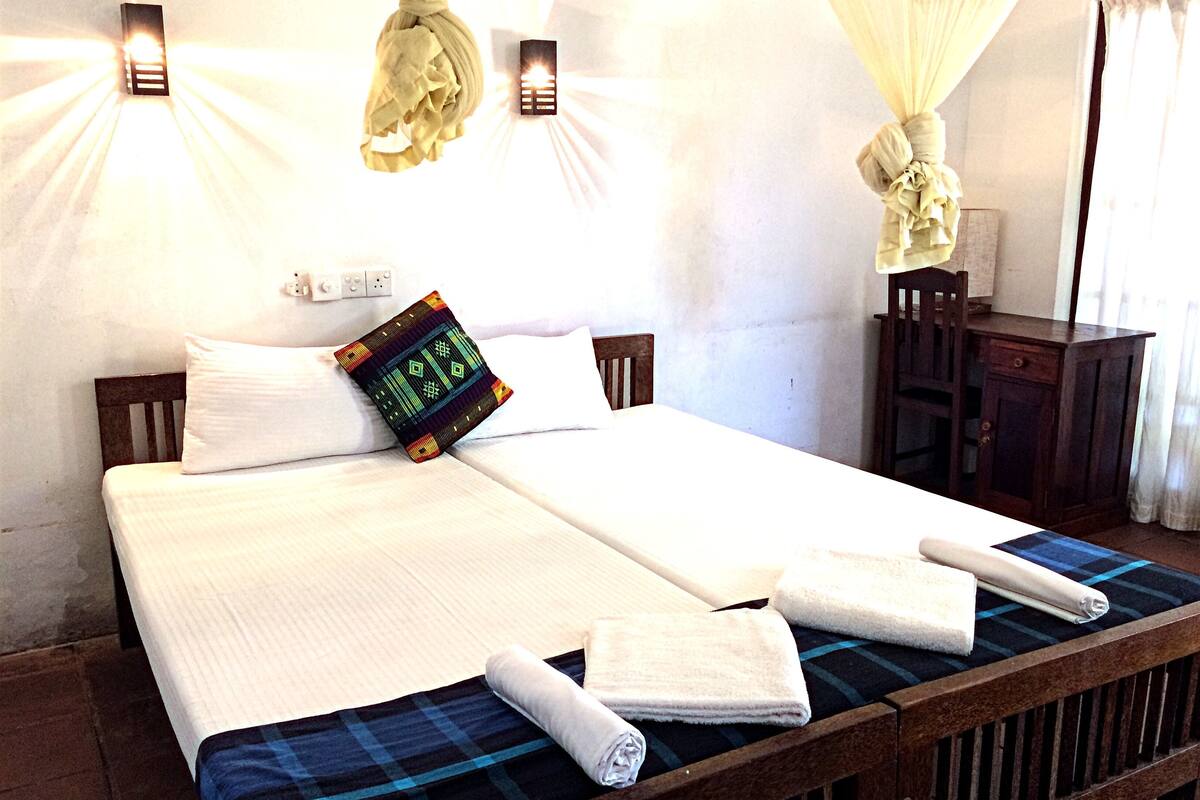 A neatly made bed with white linens, a digital clock, and towels on a checkered bedspread.