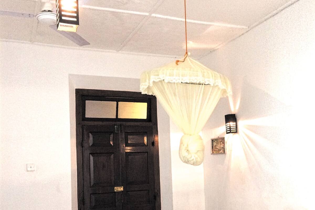 A room with a bed, a black door, a ceiling fan, and a hanging light fixture.