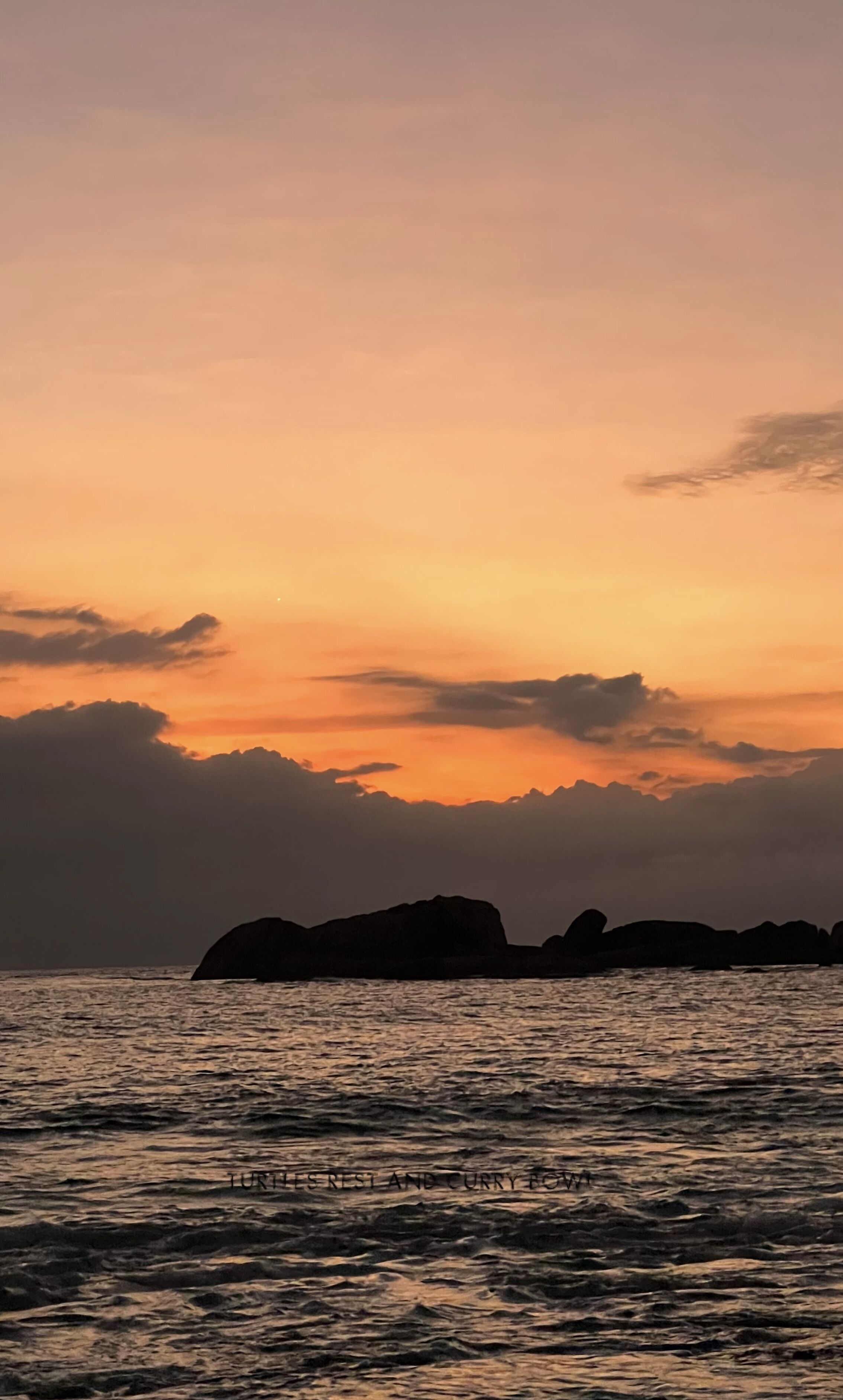 Een kustzonsondergang met rustig water en veraf gelegen rotsformaties.