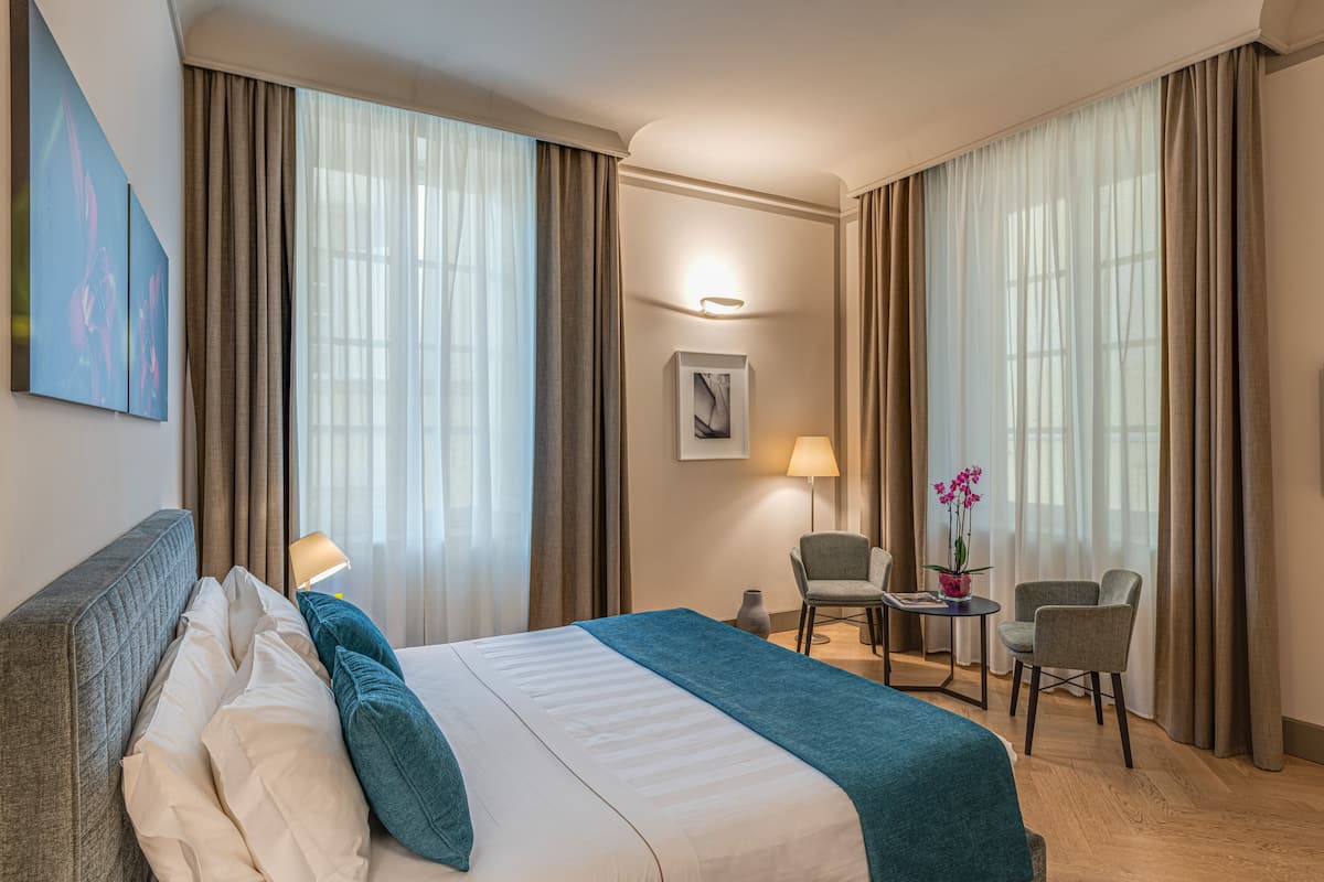 Una habitación de hotel con una cama, dos sillas, una mesita y una lámpara.