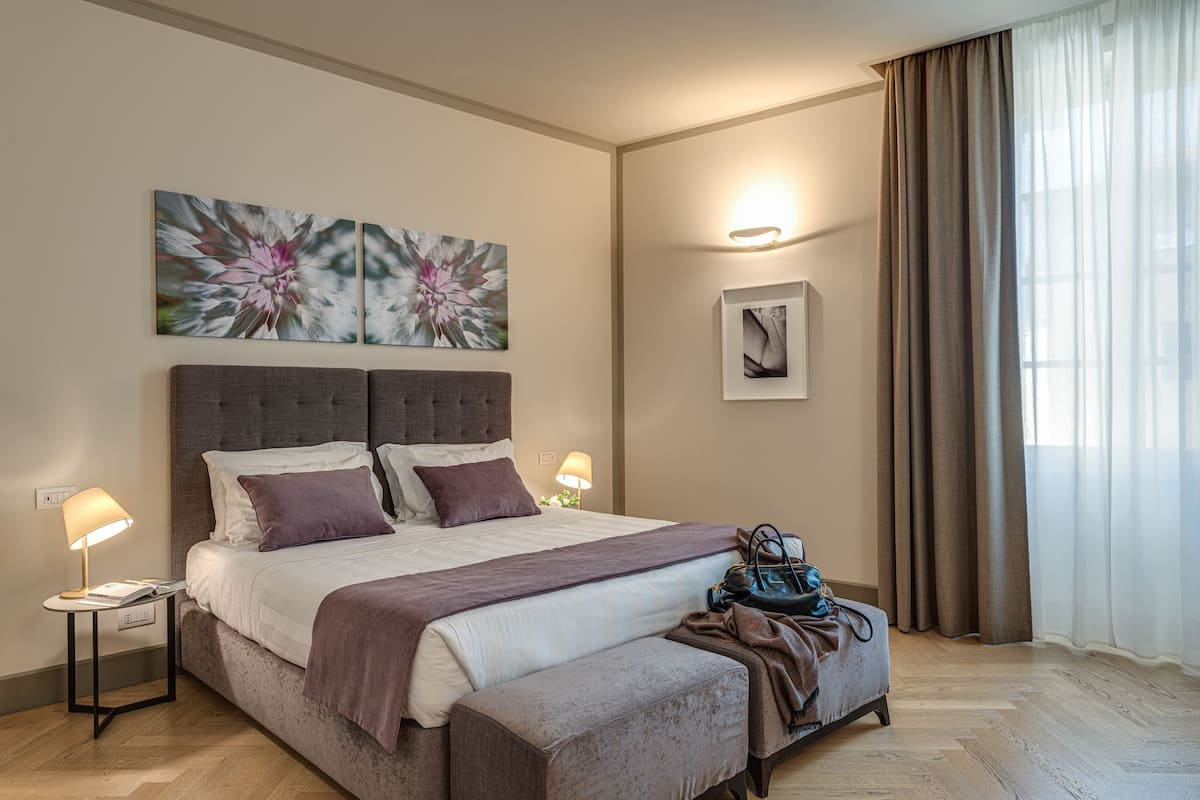 Un dormitorio moderno con una cama grande, lámparas de noche, un banco y una obra de arte en la pared.