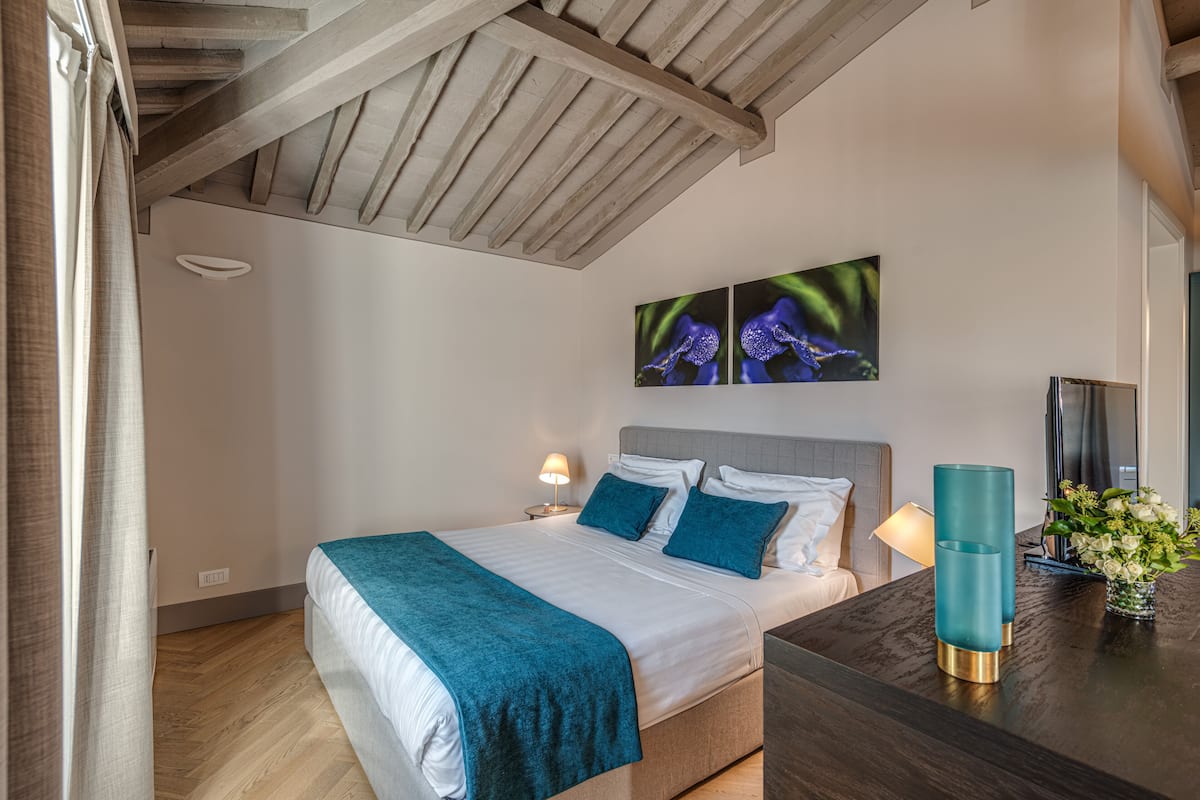 Un dormitorio con una cama, una mesita de noche, una lámpara y un florero con flores.
