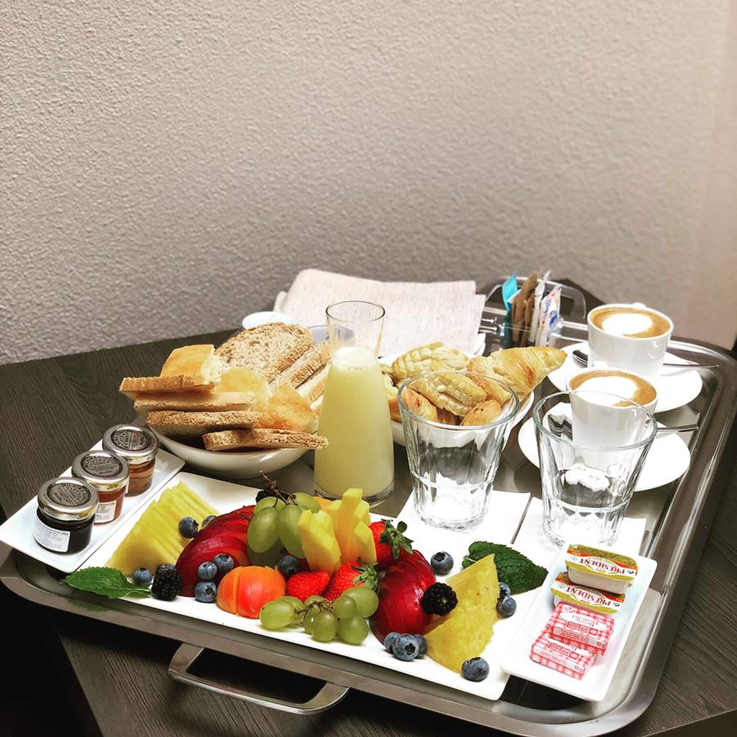 Bandeja de desayuno con pan, bollería, fruta, jugo y café.