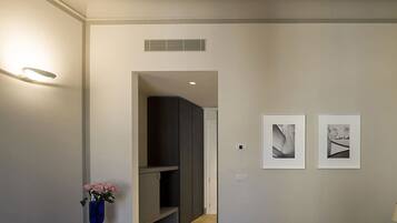 Una habitación de hotel moderna con un diseño minimalista, que presenta un mueble de madera oscura, una pequeña mesa con un jarrón de flores y dos obras de arte enmarcadas en la pared.