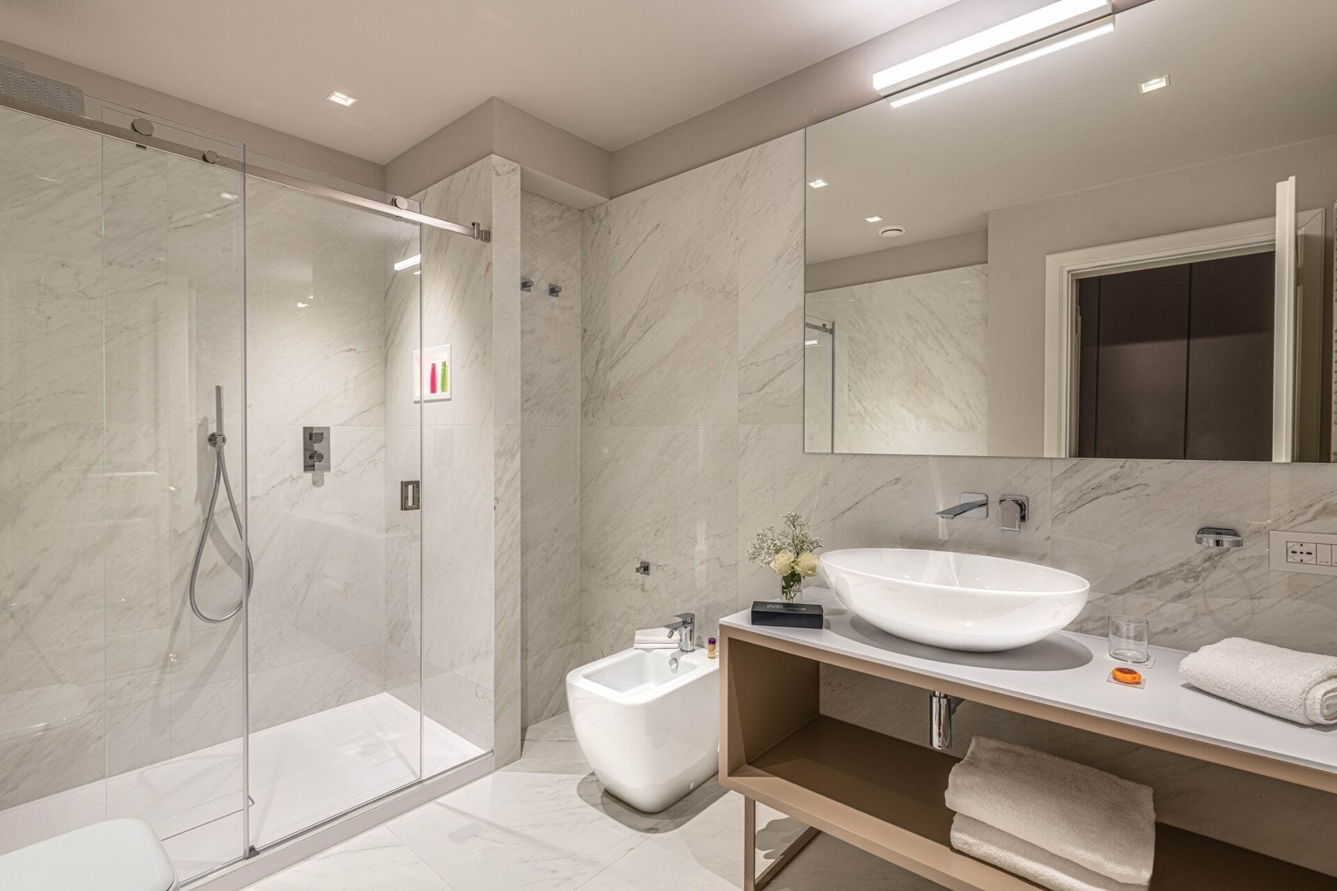 A modern bathroom with a glass-enclosed shower, a freestanding bathtub, and a large mirror above the sink.