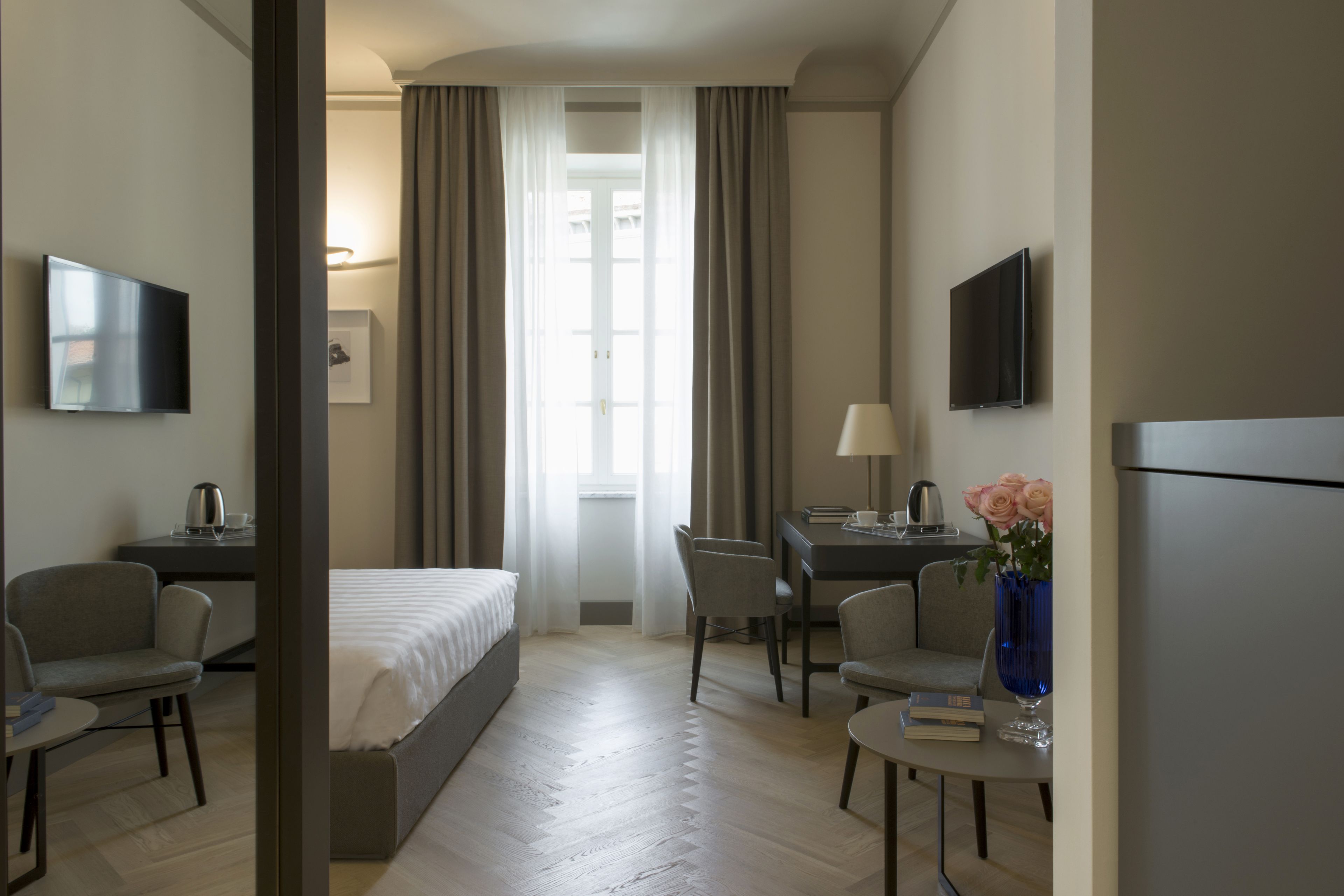 Una habitación de hotel con cama, escritorio, silla, televisor y un jarrón con flores.