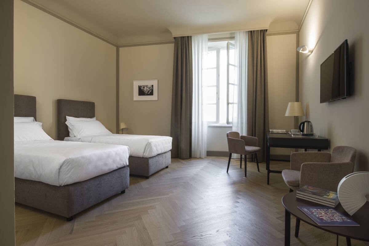 Habitación de hotel con dos camas, un escritorio, una silla y un televisor.