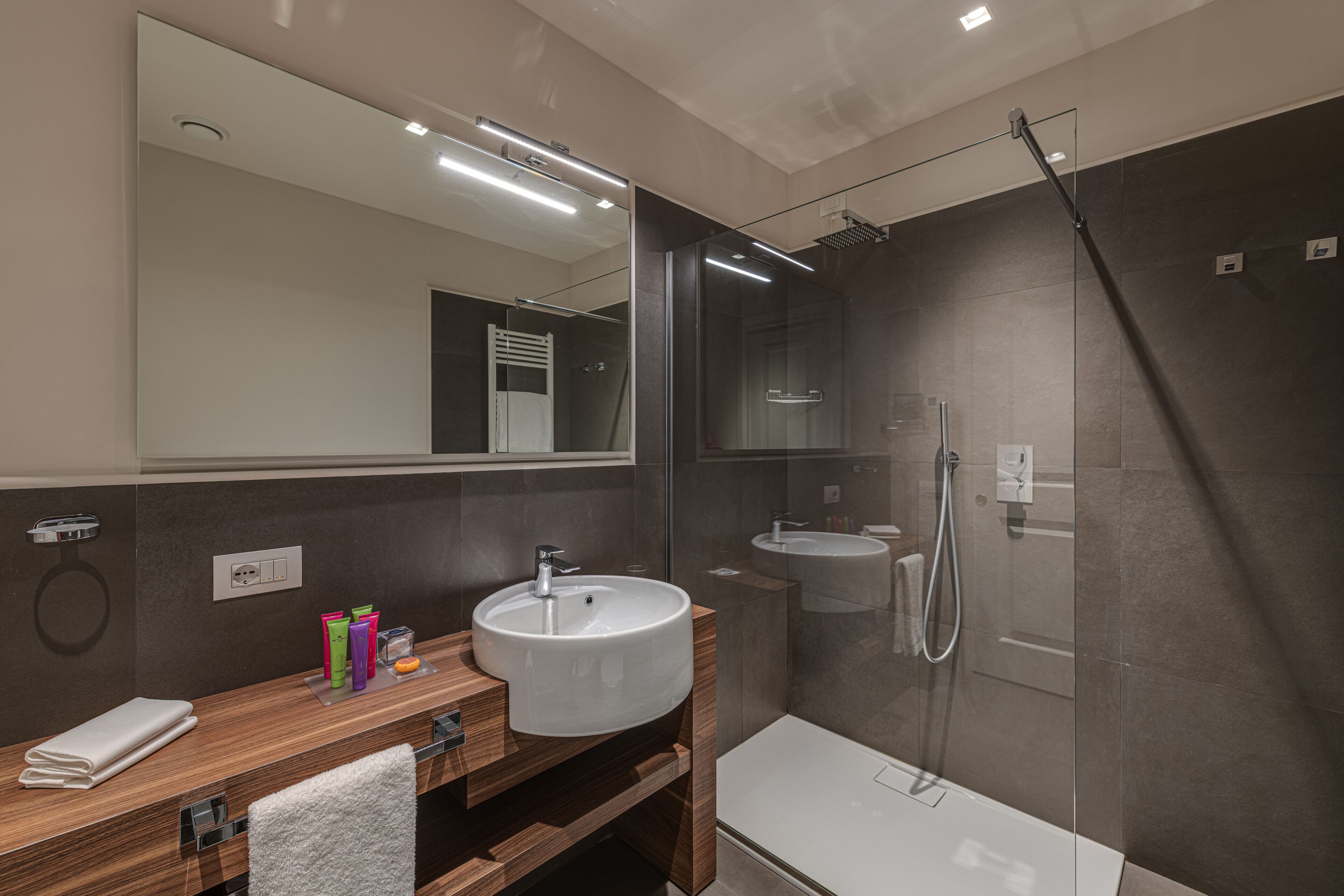 A modern bathroom with a wooden vanity, a large mirror, a glass-enclosed shower, and a white bathtub.