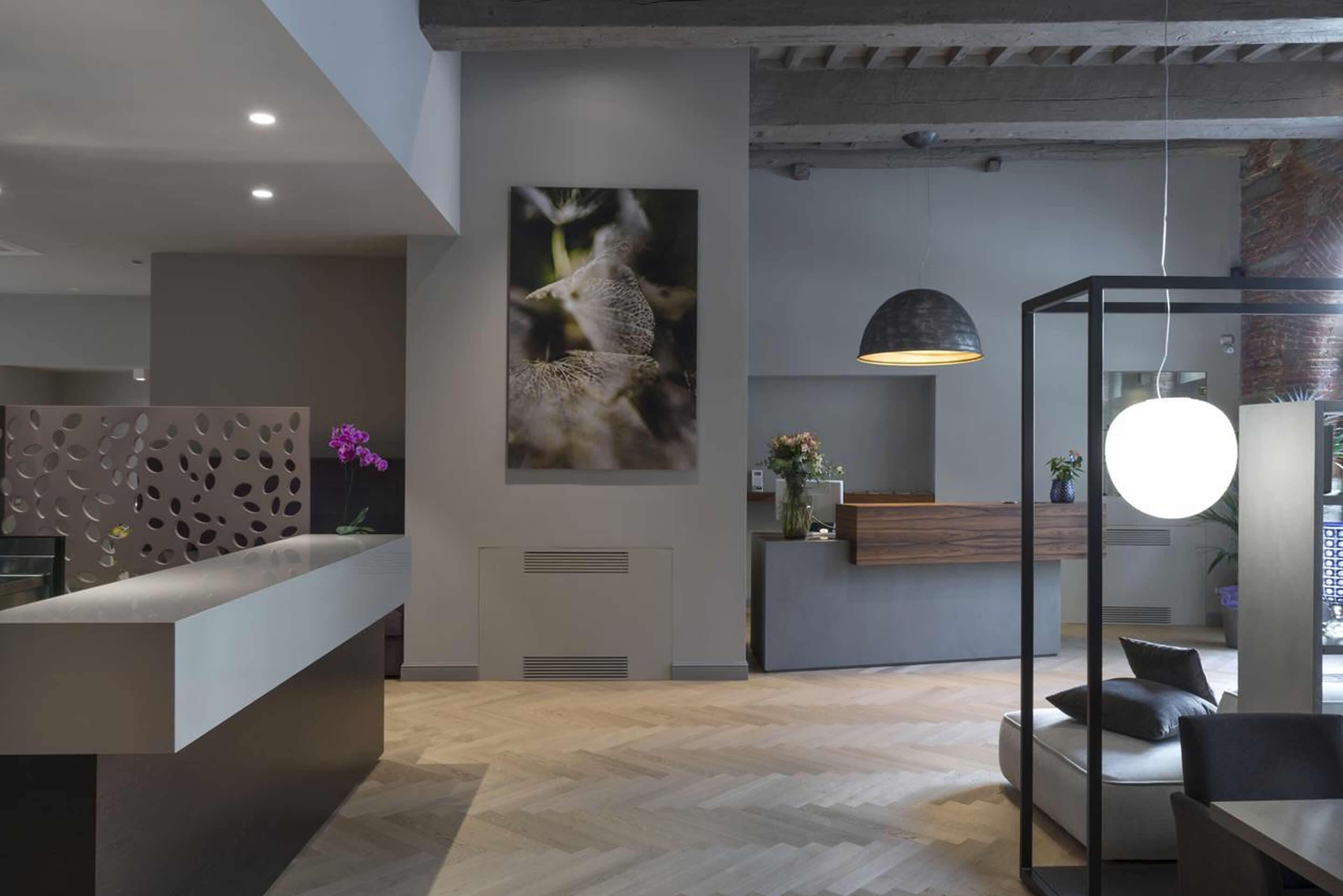 A modern reception area with a wooden reception desk, a large wall-mounted photograph, and a hanging pendant light.