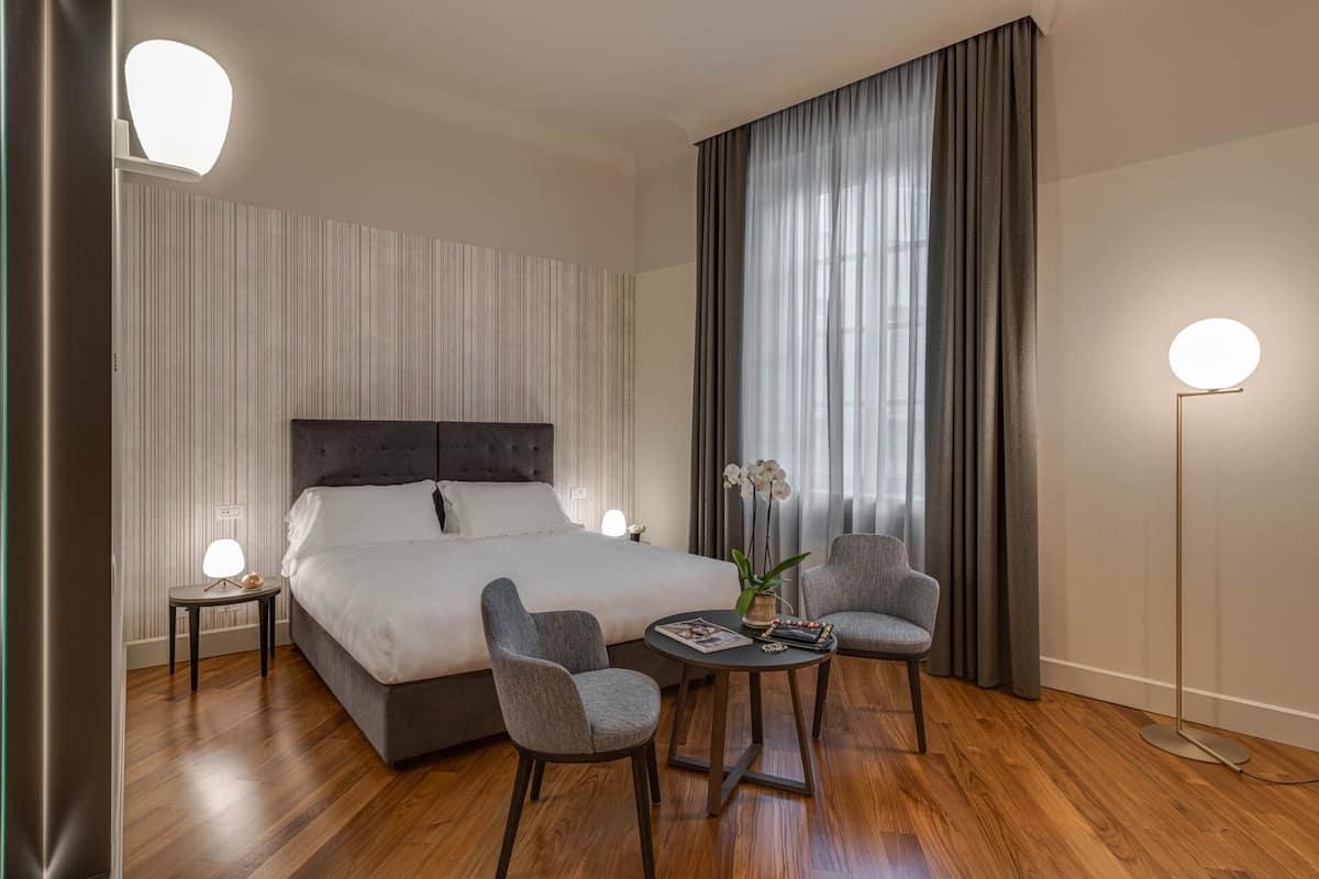 Habitación de hotel con una cama grande, dos sillones, una mesita y una lámpara de pie.