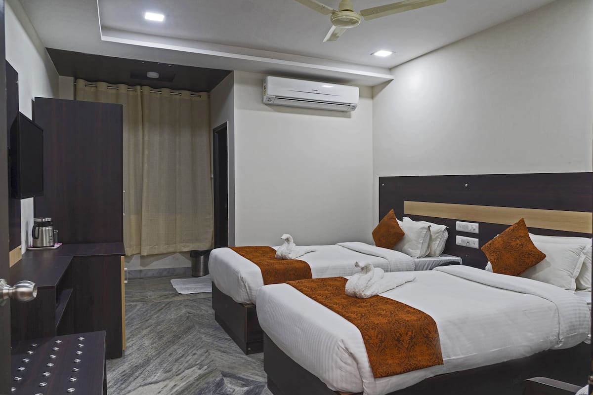 Habitación de hotel con dos camas, televisor de pantalla plana, equipo de aire acondicionado y ventilador de techo.