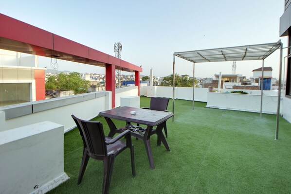Een terras op het dak met een tafel en stoelen, kunstgras, een rode luifel en uitzicht op de stads skyline.
