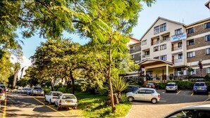 Een hotel met meerdere verdiepingen, een parkeerplaats en omringende bomen en groen.