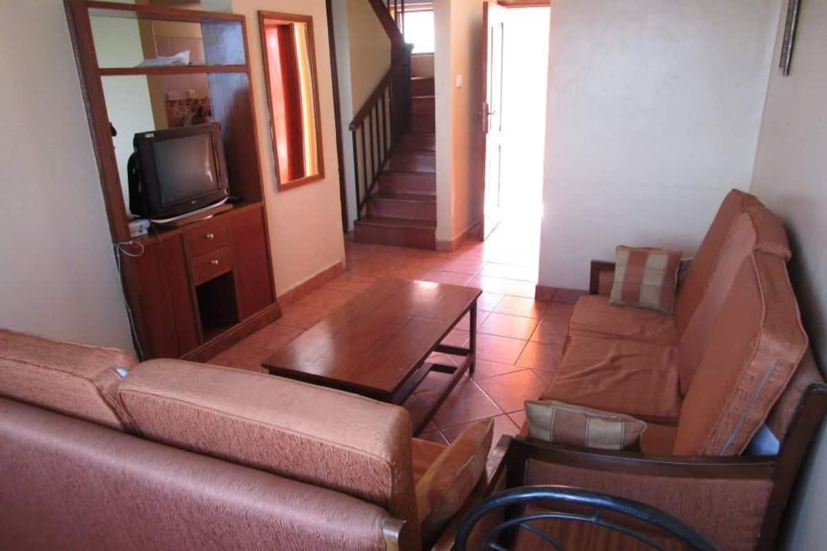 Ein Wohnzimmer mit einer Couch, einem Couchtisch, einem Fernseher auf einer Holzkommode und einer Treppe, die zu einer anderen Etage führt.