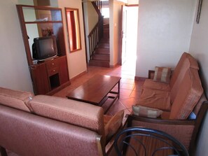 Un soggiorno con divano, tavolino, televisore su un mobile in legno e una scala che conduce a un altro piano.