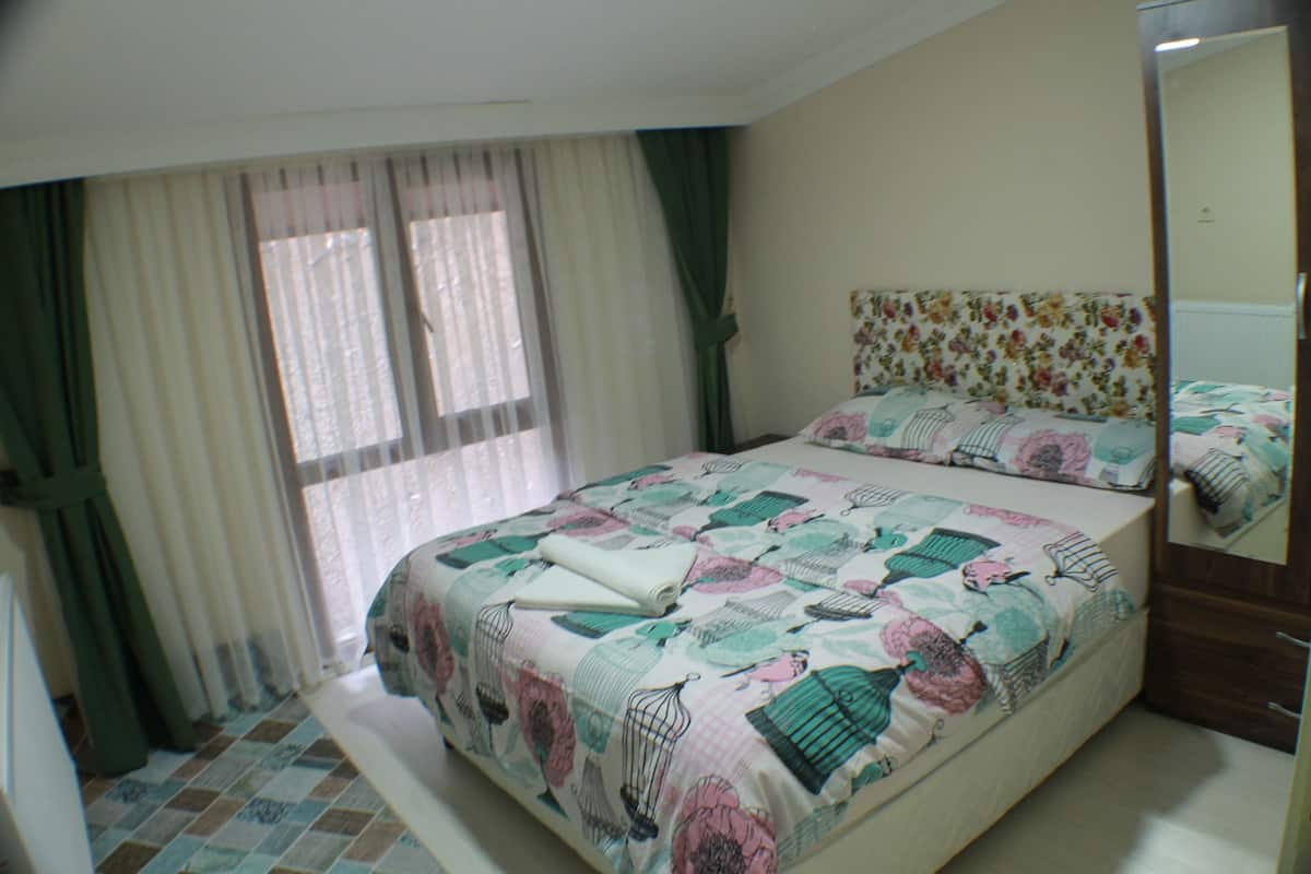 Ein Schlafzimmer mit einem Bett, Vorhängen, einem Spiegel und einem blumengemusterten Kopfteil.