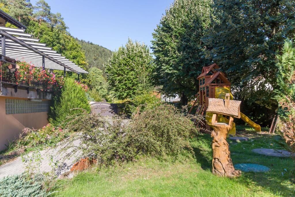 A residential area with a wooden play structure, a house with a sloped roof, and a garden with various plants.