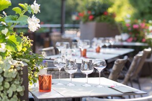 A dining table set with wine glasses and a candle, surrounded by wicker chairs and greenery. - Hôtel Restaurant Le Freudeneck (Wangenbourg-Engenthal)