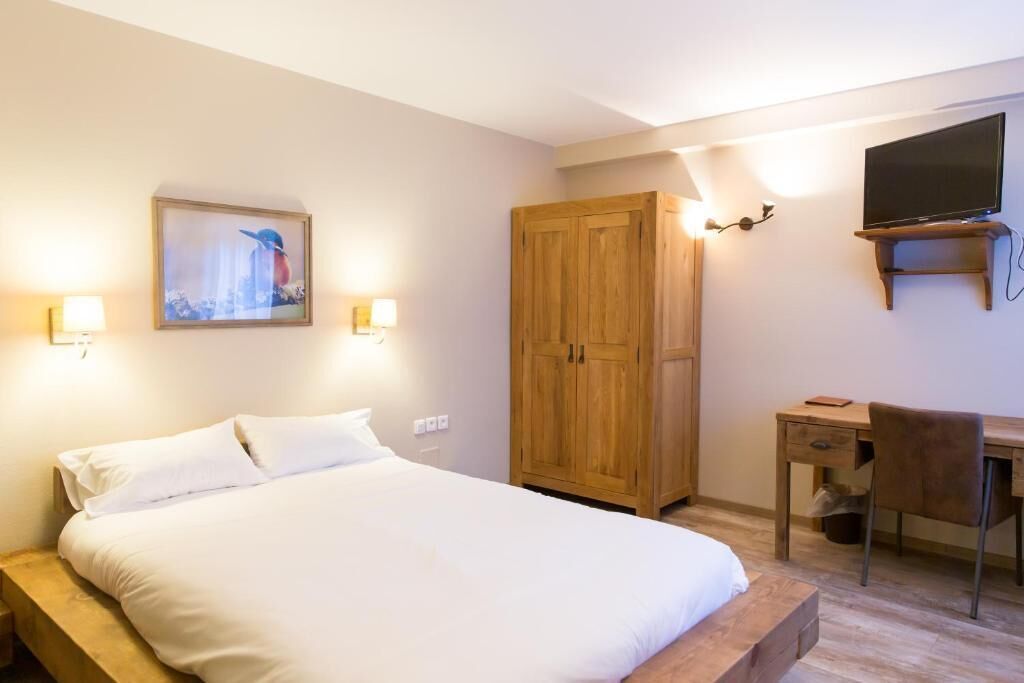 A bedroom with a bed, a wooden wardrobe, a desk with a chair, and a mounted television.