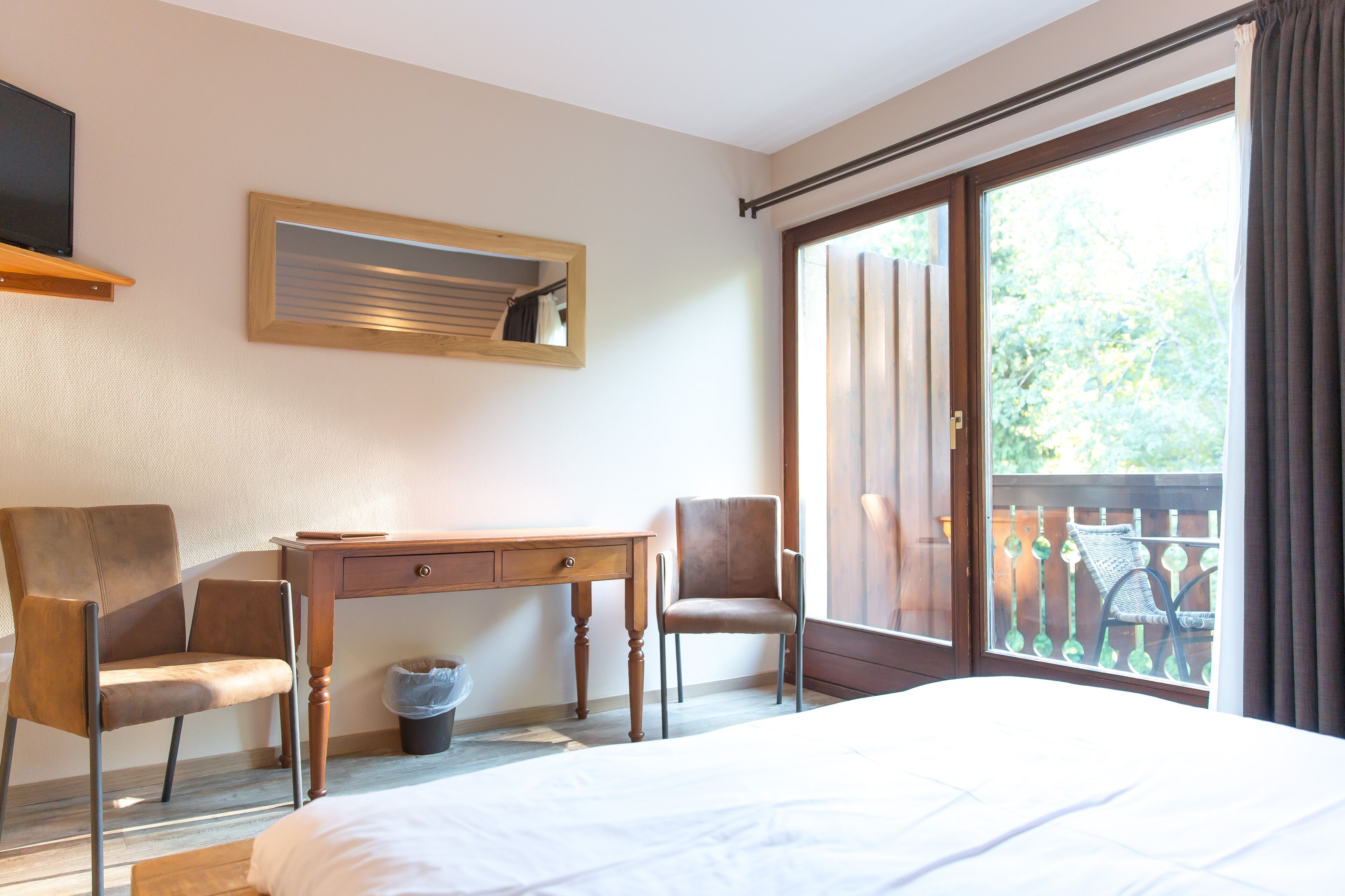 A hotel room with a bed, a desk, two chairs, a television, and a window with a view of the outdoors.