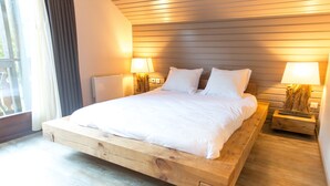 Une chambre moderne avec un lit surélevé en bois, deux tables de chevet avec des lampes et une vue sur l’extérieur.