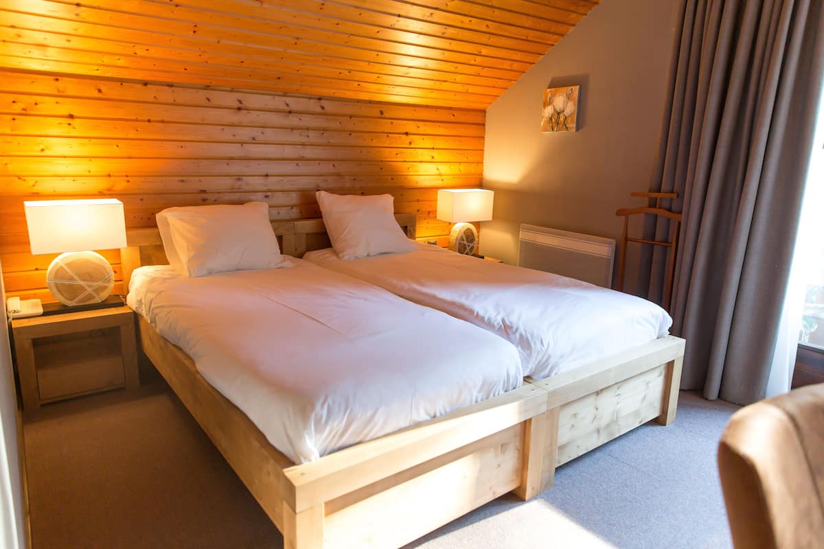 Un lit double avec une tête de lit et un pied de lit en bois, deux tables de chevet avec des lampes, un radiateur et une fenêtre avec des rideaux.