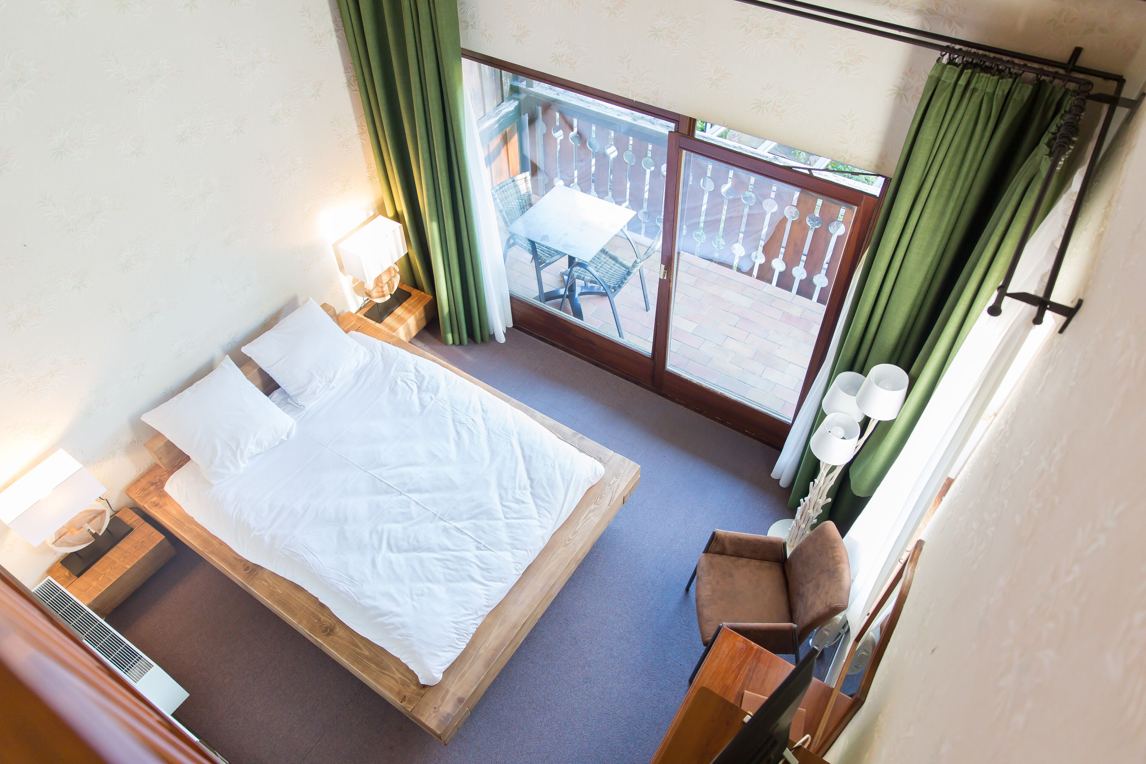 A bedroom with a large bed, a wooden nightstand, a chair, and a balcony with a table and chairs.