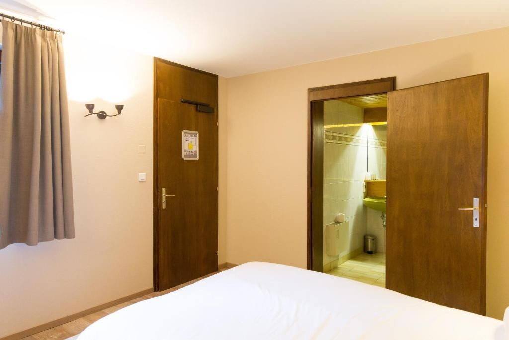 Una habitación de hotel con una cama, una puerta que da a un baño y una cortina en la ventana.