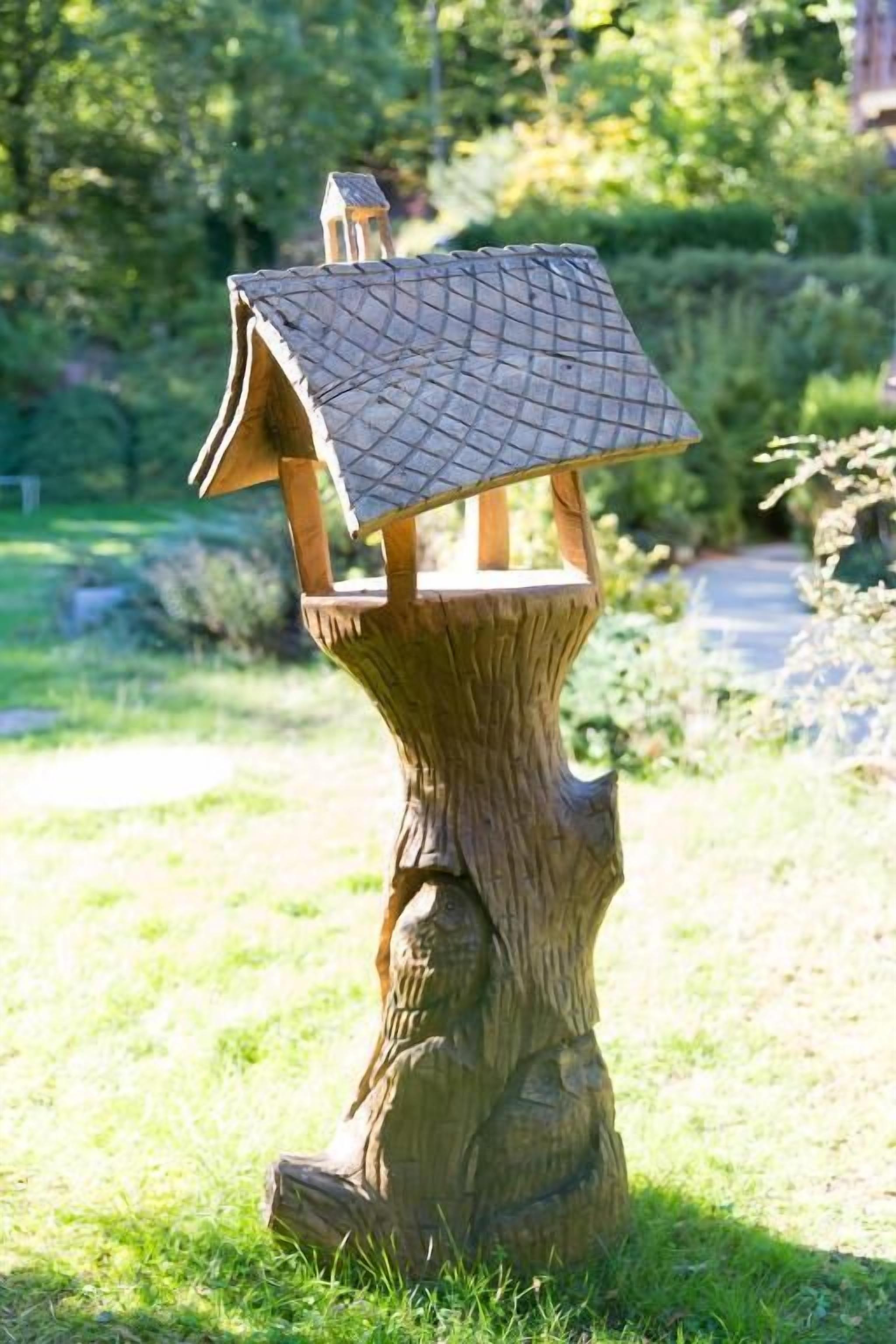 Ein Vogelhaus aus Holz auf einem Baumstumpf in einem Garten.