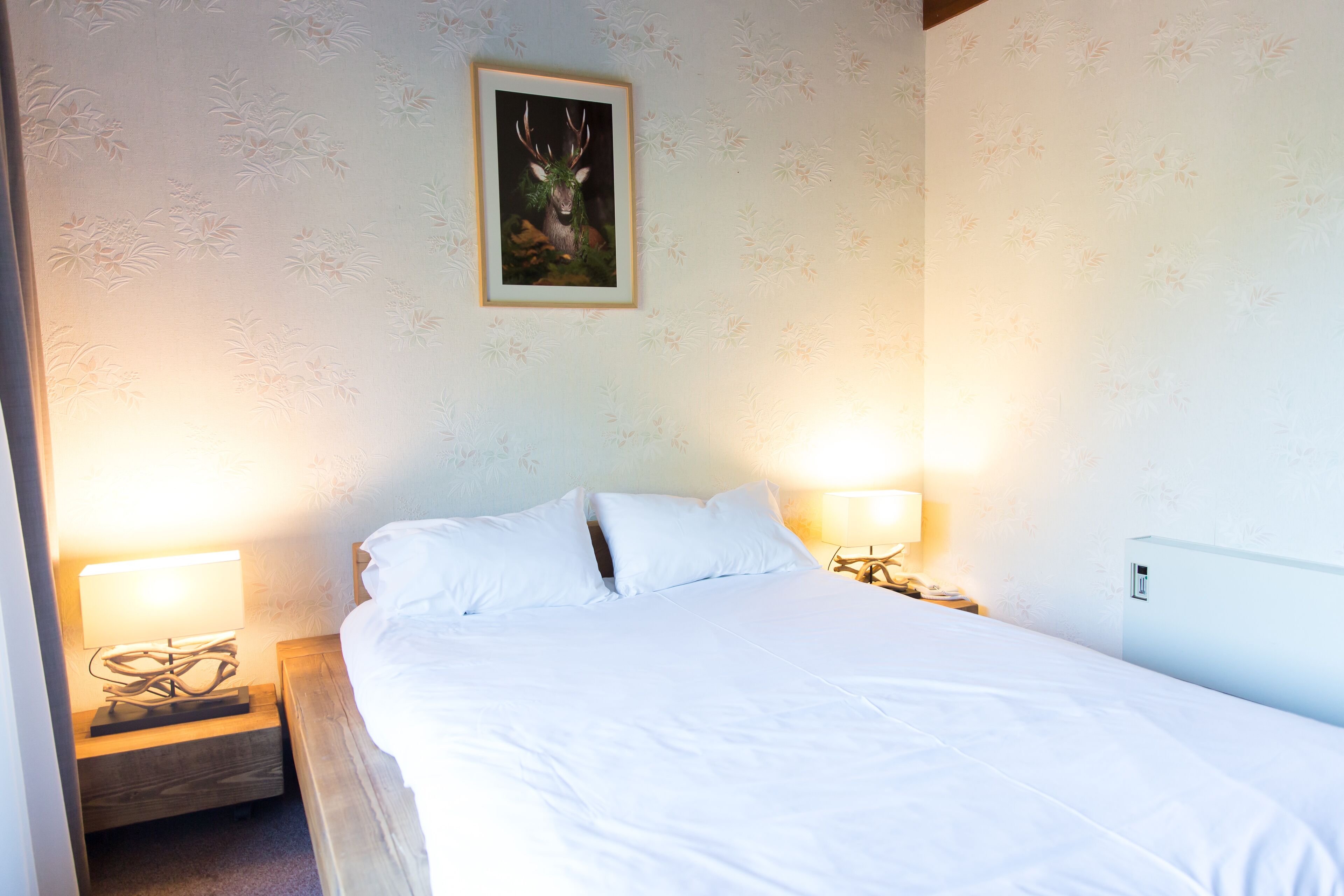 A neatly made bed with white linens, two bedside lamps, and a framed picture on the wall.