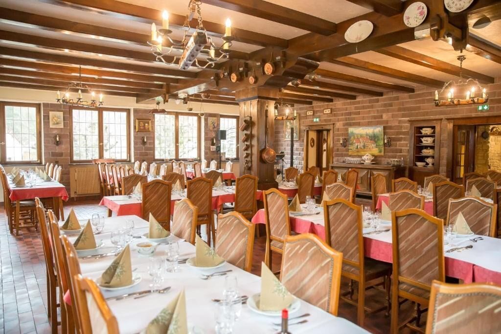 A restaurant with multiple dining tables set with white tablecloths and gold napkins, wooden chairs, and a brick wall interior.