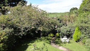 A garden with a pathway, a table and chairs, and dense foliage.