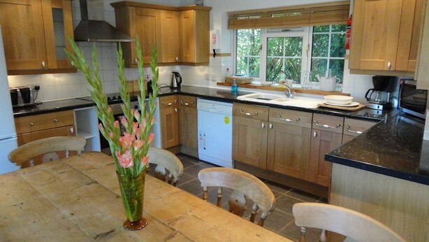 A modern kitchen with wooden cabinets, a central island, a dining table, and a window with a view of greenery.