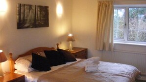 A neatly made bed with a white comforter and pillows, a bedside lamp, a nightstand, and a painting on the wall.