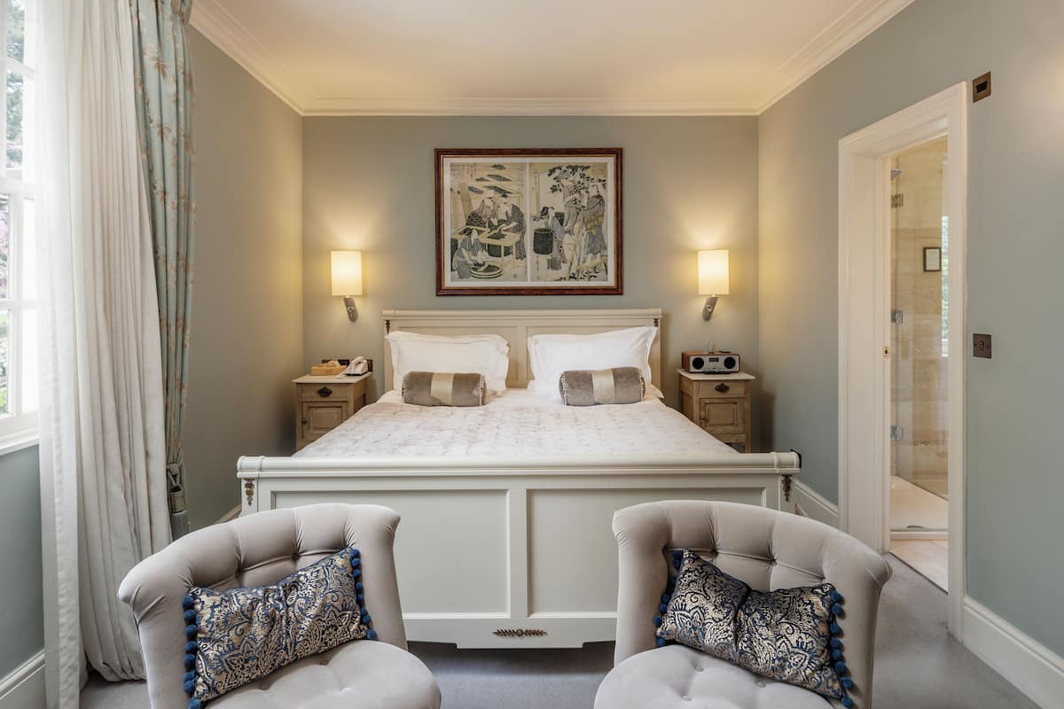 A bedroom with a large bed, two bedside tables, a framed artwork above the bed, and a door to the right.