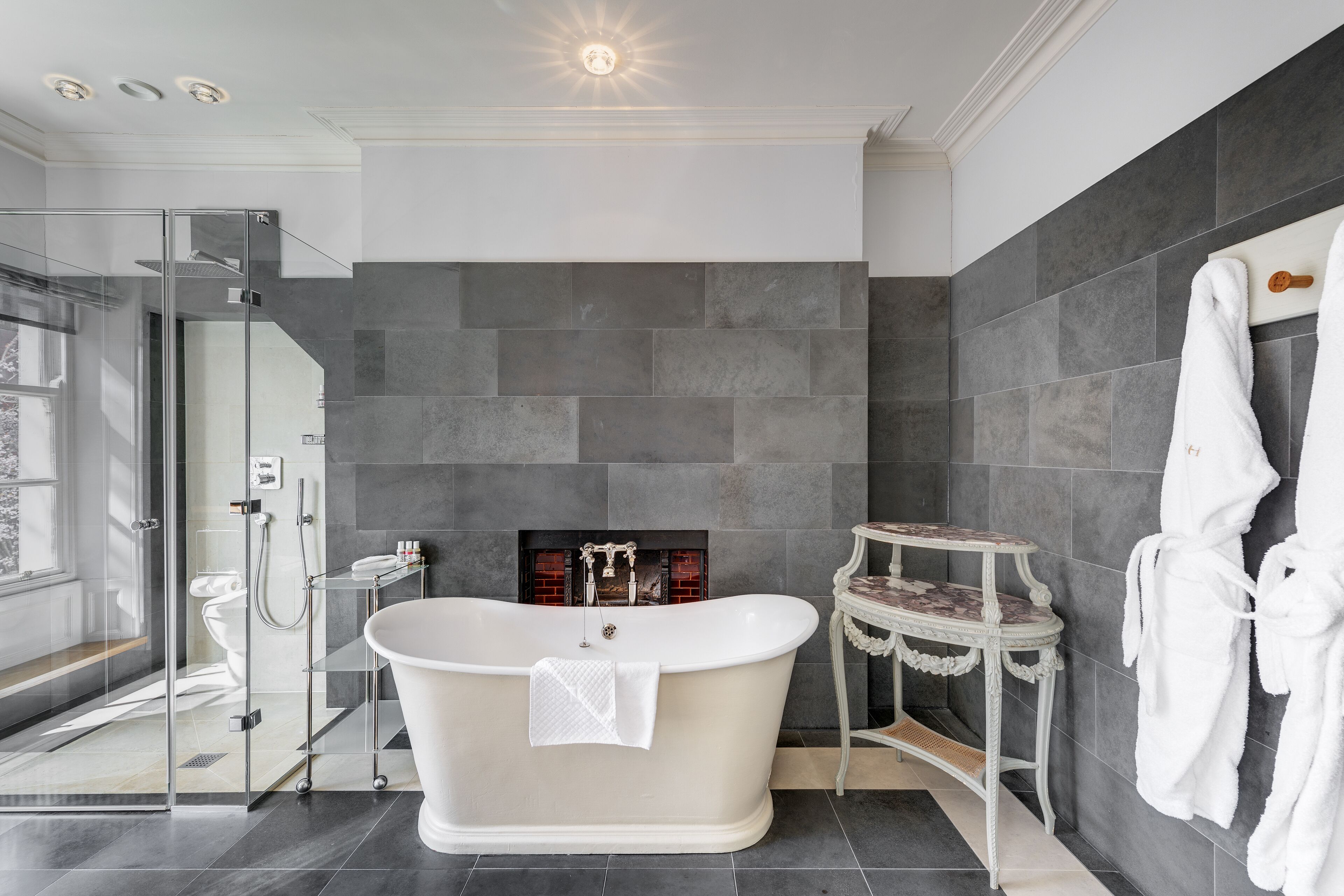 A modern bathroom with a freestanding bathtub, a glass-enclosed shower, and a marble-tiled floor.