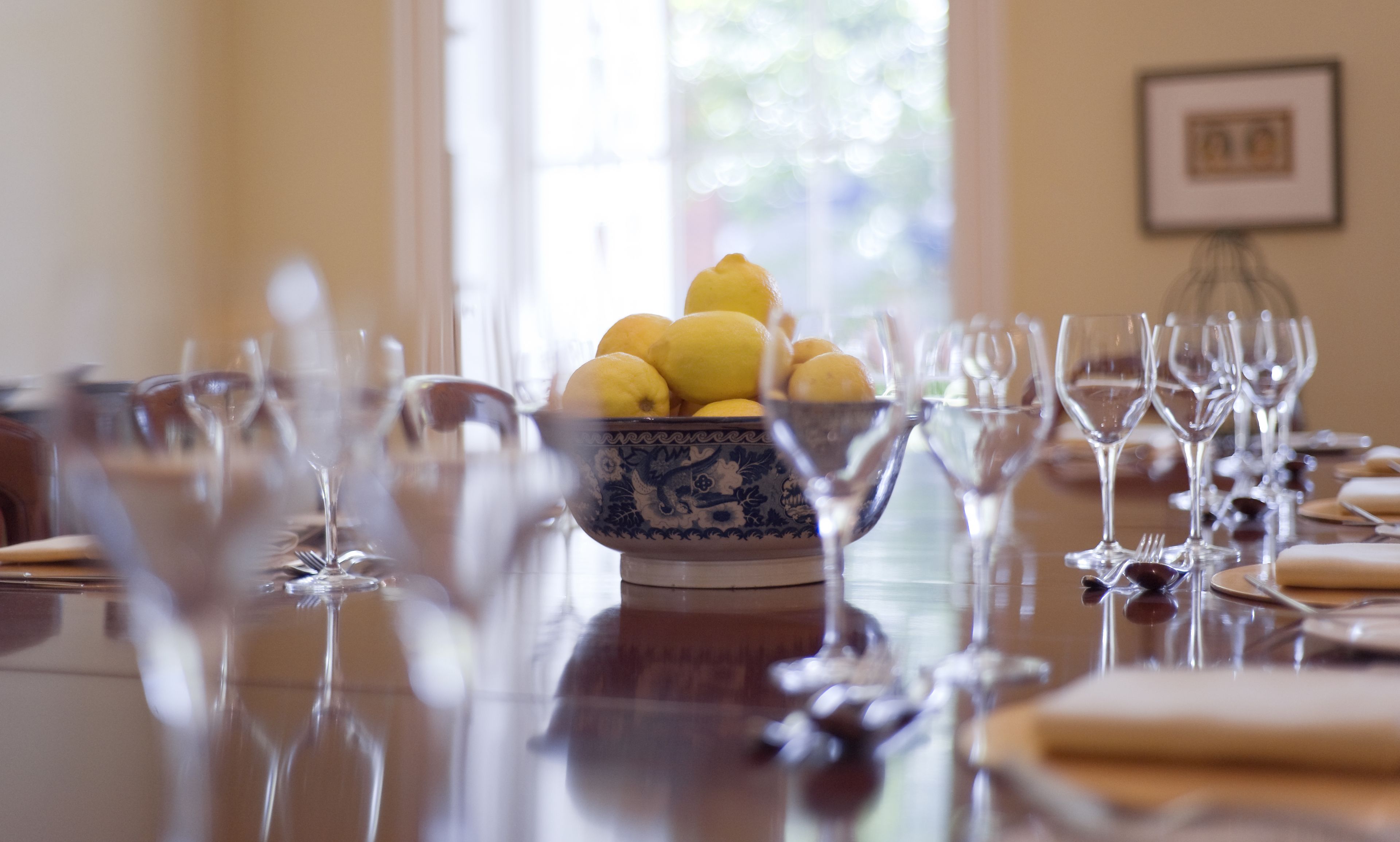 Una mesa de comedor con un bol de limones y varios vasos de vino.
