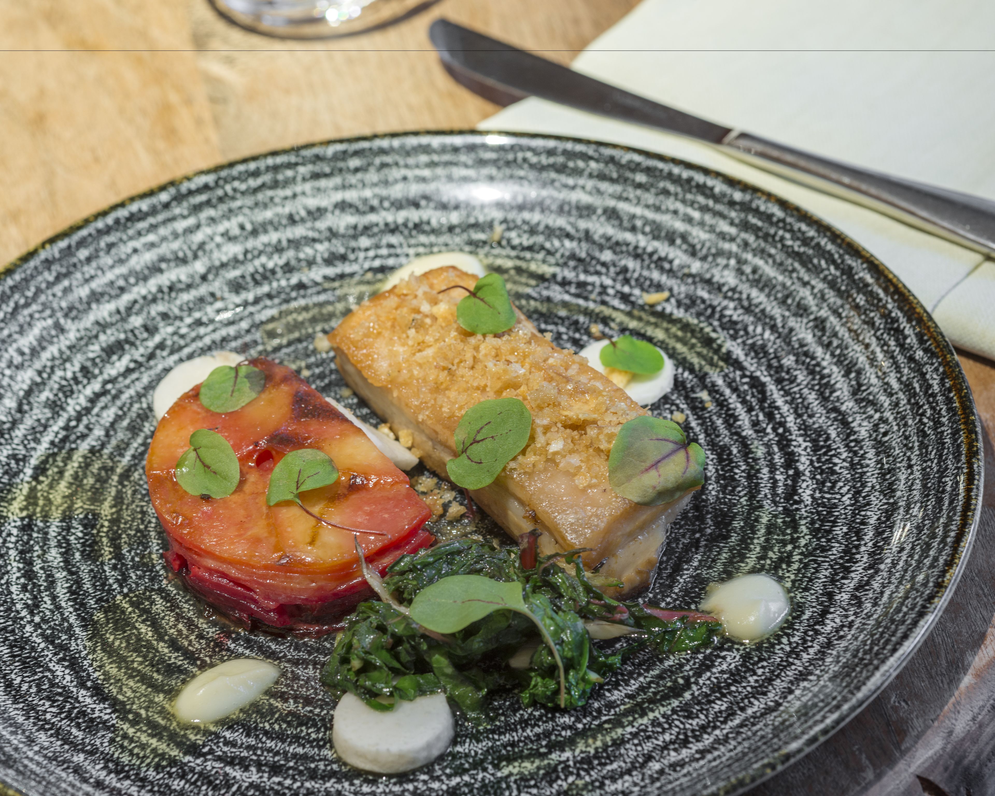 A plate with a piece of fish, a slice of tomato, and some greens.