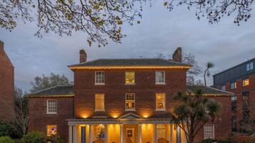 Stately brick building with a central entrance and columns, set amidst a well-manicured lawn and formal surroundings.