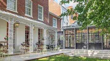 A courtyard with outdoor seating, a glass conservatory, and a brick building with white trim.